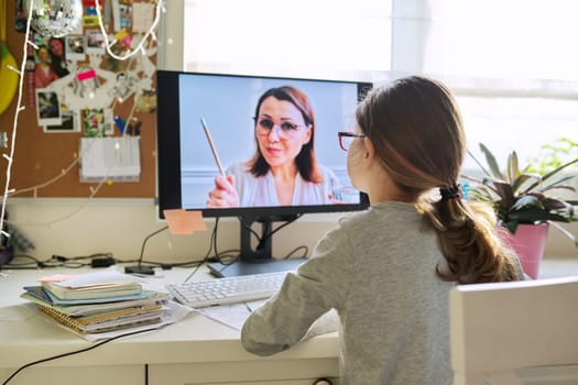 Child girl studying at home online using computer. Woman teacher on computer screen teaching little student. Virtual lesson, distance learning, e-learning, video conference, technology in education.