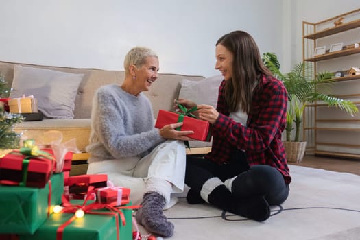 Cute young woman holds a gift box to surprise his mother on Christmas Day. 60 year old retired woman happy Happy daughter on Christmas day in living room holding red gift box.