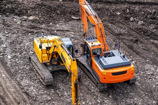 A yellow excavator works in the mountains. Construction of roads and houses in beautiful mountains.