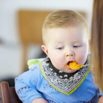 Toddler, eating and meal with spoon in kitchen for lunch with baby food, carrot or squash. Little boy, infant or hungry for delicious, yummy and health in home for future, growth or child development.