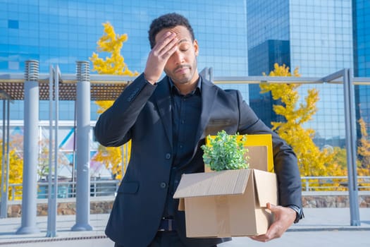 Businessman fired with cardboard box with office supplies standing sad outside office building. High quality photo