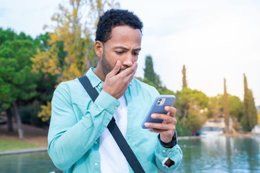 Student looking at the phone with a surprised expression outdoors in the campus park. High quality photo