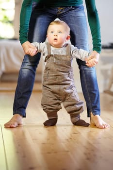 Mother, baby and helping with walking in home with support, trust and care for childhood development. Toddler, little boy and holding hand for motor skills, assistance and mobility in living room.