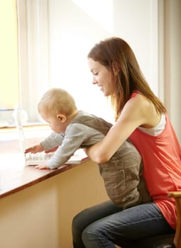 Mother, holding and baby with laptop in home for remote, work or bond with child in kitchen. Young woman, parenting and son by smile for growth, milestone or development for care, love and support.