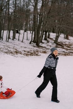 Happy mother carries a small child in a sleigh on a snowy slope. High quality photo