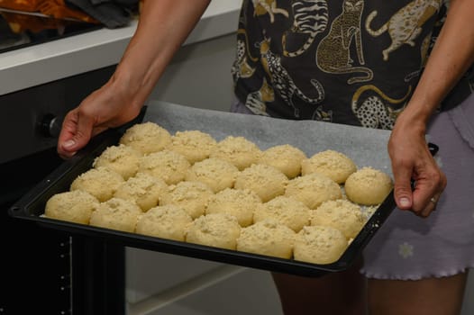 woman puts buns in the oven on a baking sheet