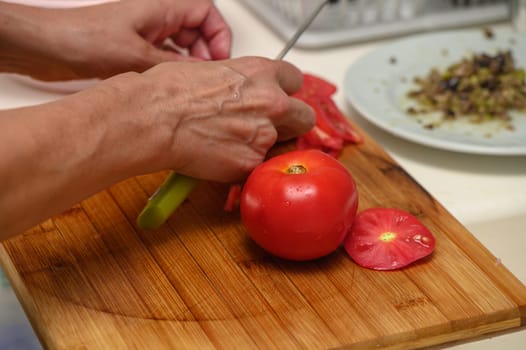 woman cutting tomato on kitchen board