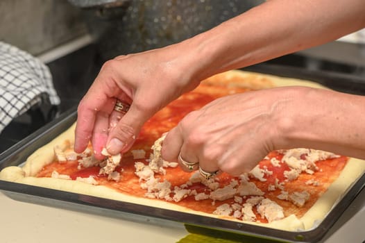 a woman prepares pizza with cheese, tomatoes and chicken ham, a woman lays out chicken ham
