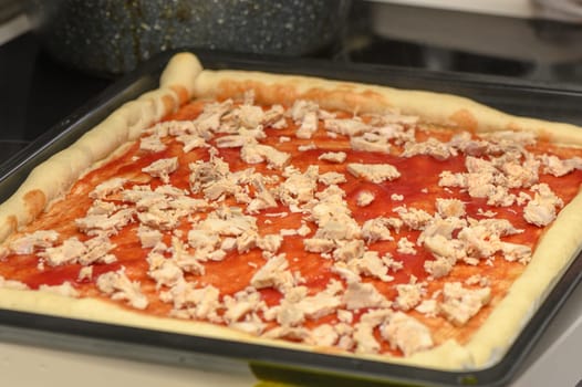 a woman prepares pizza with cheese, tomatoes and chicken ham, a woman lays out chicken ham 2