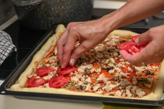 a woman prepares pizza with cheese, tomatoes and chicken ham, a woman lays out tomatoes