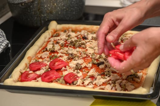 a woman prepares pizza with cheese, tomatoes and chicken ham, a woman lays out tomatoes 1