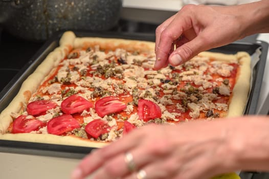 a woman prepares pizza with cheese, tomatoes and chicken ham, a woman lays out tomatoes 2