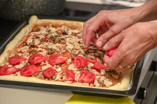 a woman prepares pizza with cheese, tomatoes and chicken ham, a woman lays out tomatoes 3