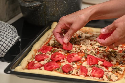 a woman prepares pizza with cheese, tomatoes and chicken ham, a woman lays out tomatoes 4