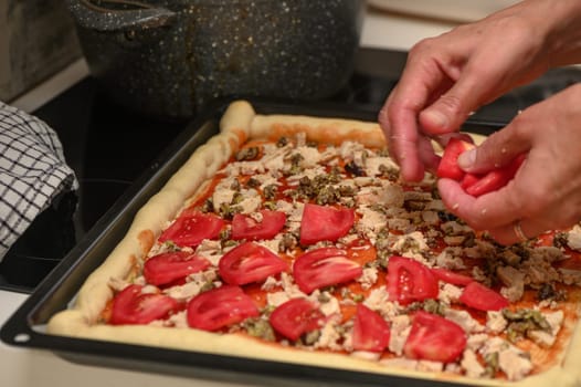 a woman prepares pizza with cheese, tomatoes and chicken ham, a woman lays out tomatoes 5
