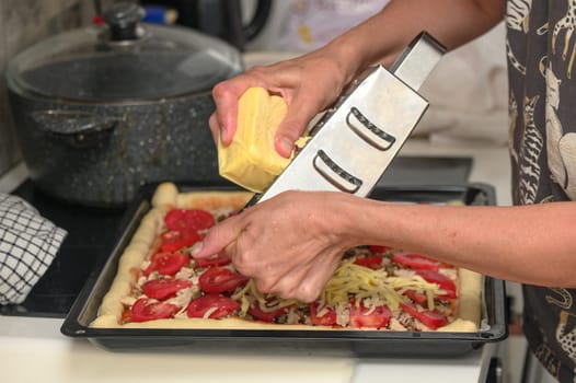 woman prepares pizza with cheese, tomatoes and chicken ham, woman rubs cheese 1