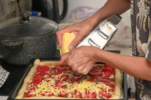 woman prepares pizza with cheese, tomatoes and chicken ham, woman rubs cheese 2