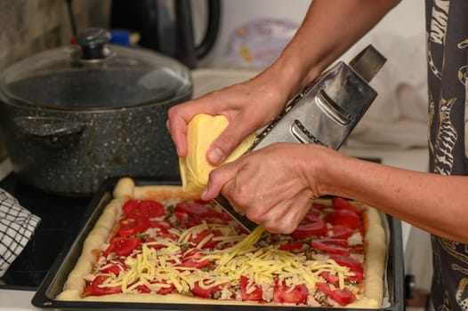 woman prepares pizza with cheese, tomatoes and chicken ham, woman rubs cheese 3
