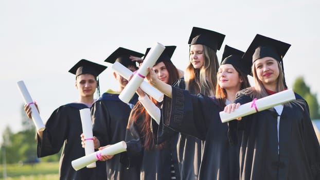 Cheerful graduates waving their diplomas on a sunny day