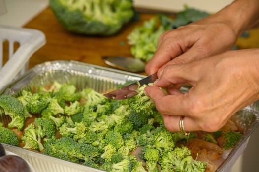 woman cutting broccoli into chicken fillet for baking 1
