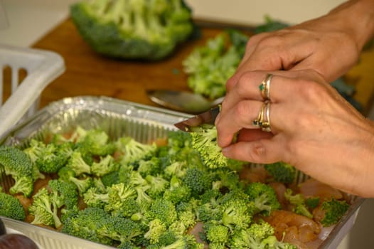 woman cutting broccoli into chicken fillet for baking