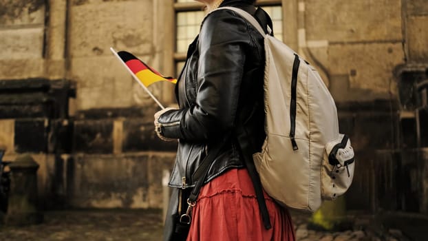 Attractive Female Tourist With Germany Flag Walks In Historical Center Of Dresden Carrying Backpack