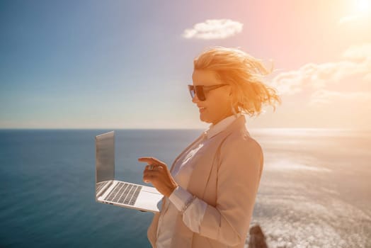 Freelance women sea working on the computer. Good looking middle aged woman typing on a laptop keyboard outdoors with a beautiful sea view. The concept of remote work