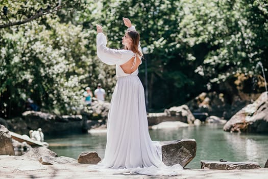 a beautiful woman in a long white dress looks into the distance at a beautiful lake with swans