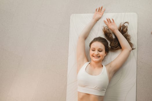 A girl in white clothes lies on a rug and laughs before yoga classes indoors.