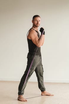 A man in black sportswear is engaged in strength fitness using a rubber loop indoors.