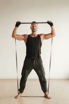 A man in black sportswear is engaged in strength fitness using a rubber loop indoors.