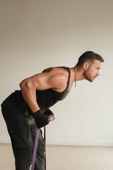 A man in black sportswear is engaged in strength fitness using a rubber loop indoors.