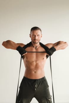 A man with a naked torso is engaged in strength fitness using a rubber loop indoors.