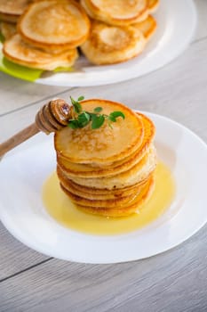 cooked sweet pancakes with honey in a plate on a light wooden table.