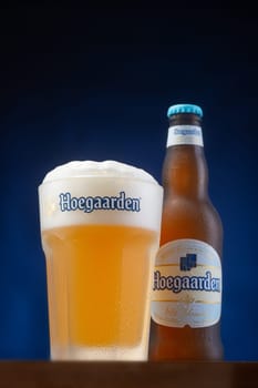 Severodonesk/Ukraine : 08.21.2021-beer Hoegaarden in a glass and bottle on a blue background