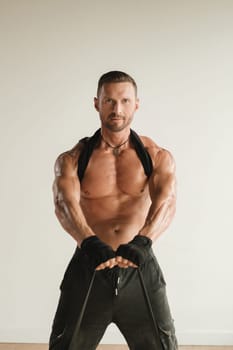 A man with a naked torso is engaged in strength fitness using a rubber loop indoors.