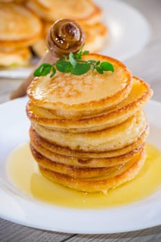cooked sweet pancakes with honey in a plate on a light wooden table.