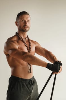 A man with a naked torso is engaged in strength fitness using a rubber loop indoors.