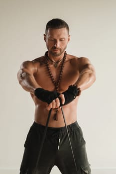 A man with a naked torso is engaged in strength fitness using a rubber loop indoors.