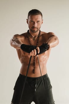 A man with a naked torso is engaged in strength fitness using a rubber loop indoors.