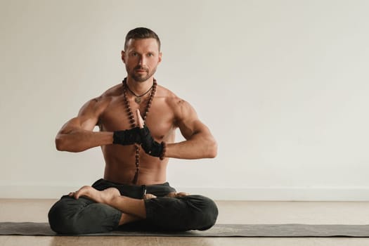 a man with a naked torso is sitting in the lotus position before doing yoga indoors. Fitness Trainer.