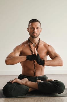 a man with a naked torso is sitting in the lotus position before doing yoga indoors. Fitness Trainer.