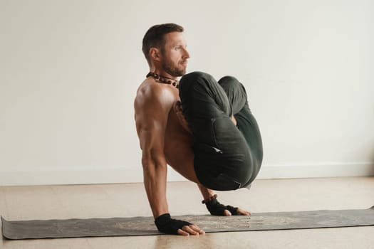 a man with a naked torso does yoga standing on his hands indoors. Fitness Trainer.