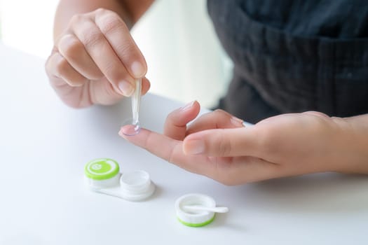 Girl puts contact lens on her index finger with tweezers. There is container for lenses nearby. Close-up, side view