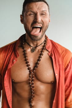 A muscular man with a naked torso in orange clothes stands in a room on a light background.