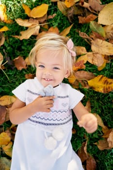 Little girl with a soft toy in her hands lies on the green grass among the yellow leaves. High quality photo