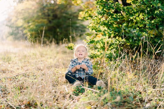 Little girl crying while sitting on a green lawn. High quality photo