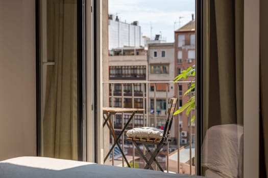 Small table and chair on sunny terrace view from renovated apartment. Simple place to rest on open balcony in residence in Barcelona city