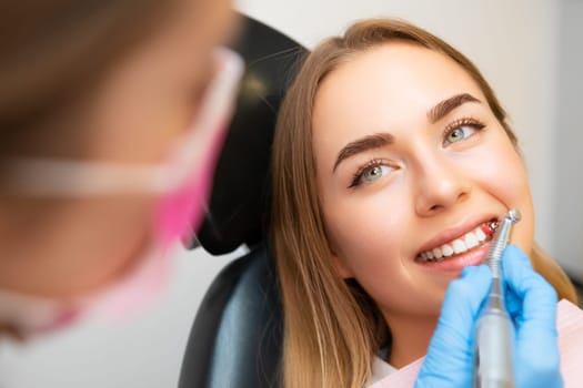 A dentist expertly conducts a teeth grinding procedure on lady in a dental clinic, enhancing her beautiful smile.