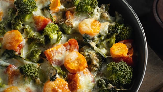 Gratin with broccoli, carrots and cheese baked in the oven on a dark wooden table, close up.